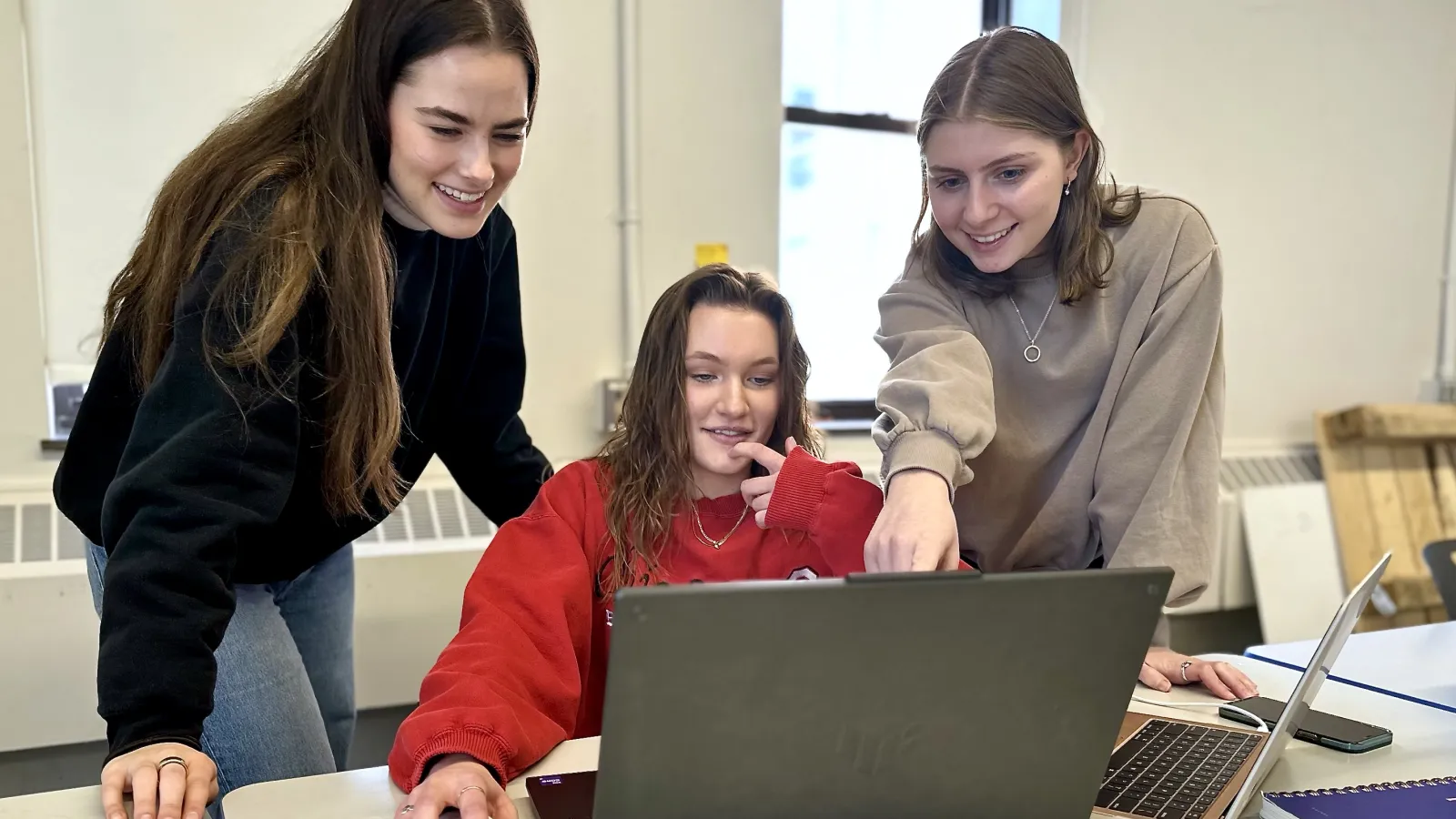Three interior design students collaborate over a laptop to design their digital poster presentation.