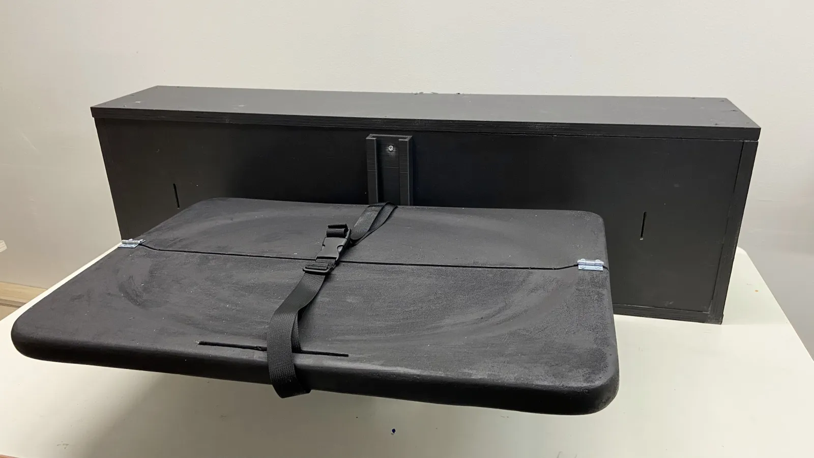 The Frunk Changing table prototype is unfolded as if you were about to change your baby. The table part is split in half long-ways, hinging so that it can fold up against the back of the frunk when not in use. The table has a buckled safety strap across the middle.
