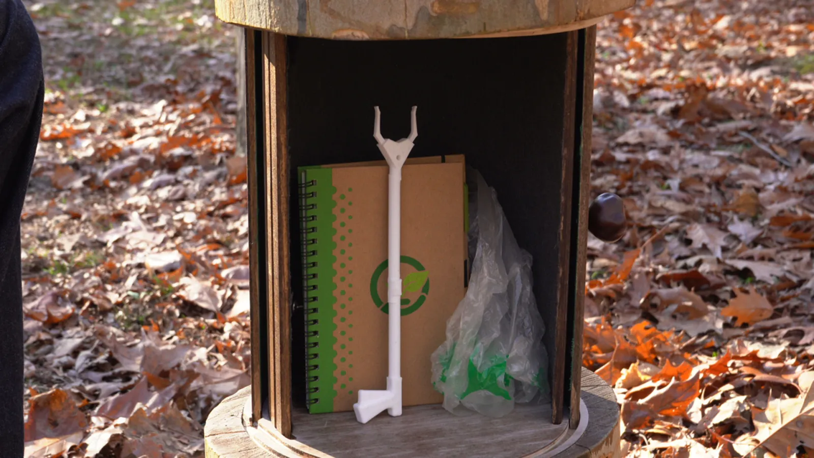 Inside the hidden compartment behind the tambour door are a logbook, a pen, a white 3D-printed trash grabber, and a trash bag.