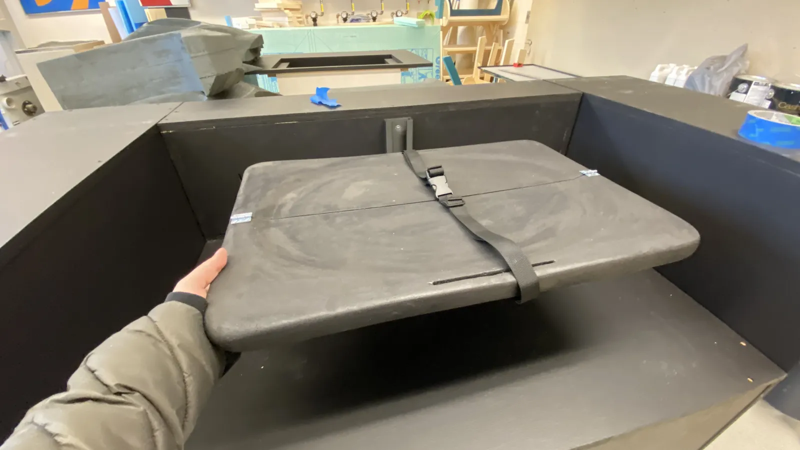 The changing table prototype is placed into the base boxes of the truck model, showing how it would proportionally fit into the space. An arm holds the bottom left corner of the table, as if the table is being unfolded and pulled out for use.