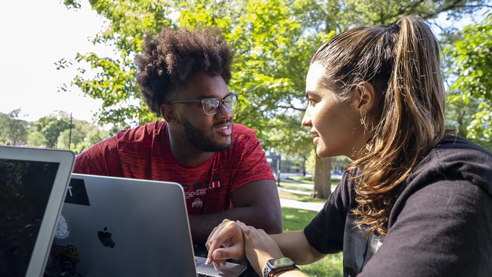 Two students outside on campus talking with a notebook computer in front of them