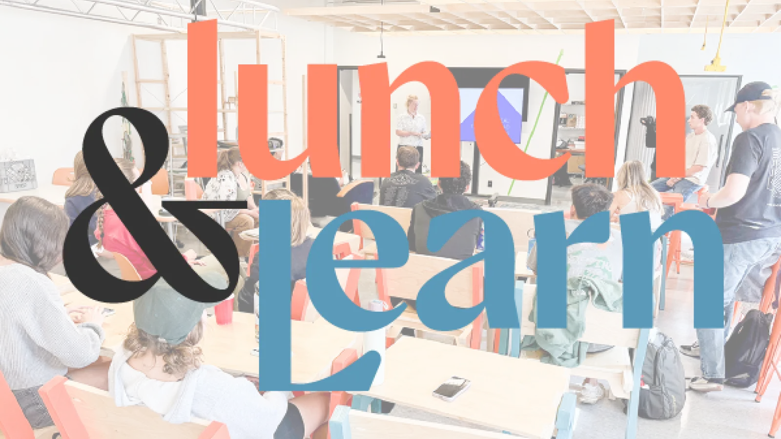 The words “lunch & learn” layered on top of a photograph of students watching a presentation in a classroom.