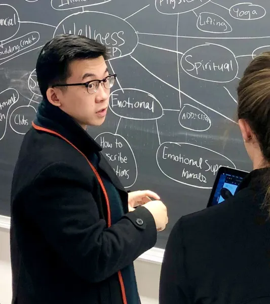 Three students collaborating in front of a chalkboard with a mind map on it.