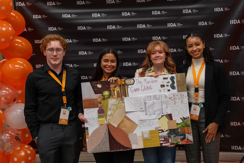 Four students displaying a design project board titled "The Meridian Care Clinic" at the IIDA Student Conference.